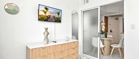 A modern bathroom with a wooden vanity, a large mirror, a wall-mounted TV, and a sliding glass door leading to a dining area.