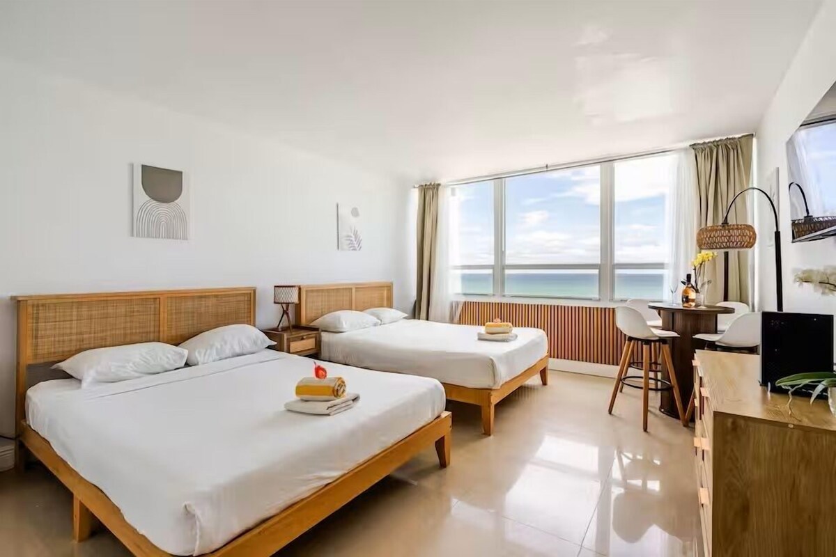 A hotel room with two beds, a desk, a chair, and a large window with a view.