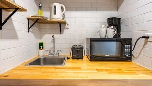 Una cucina compatta con lavello, tostapane, forno a microonde, bollitore e macchina del caffè su un piano di lavoro in legno.