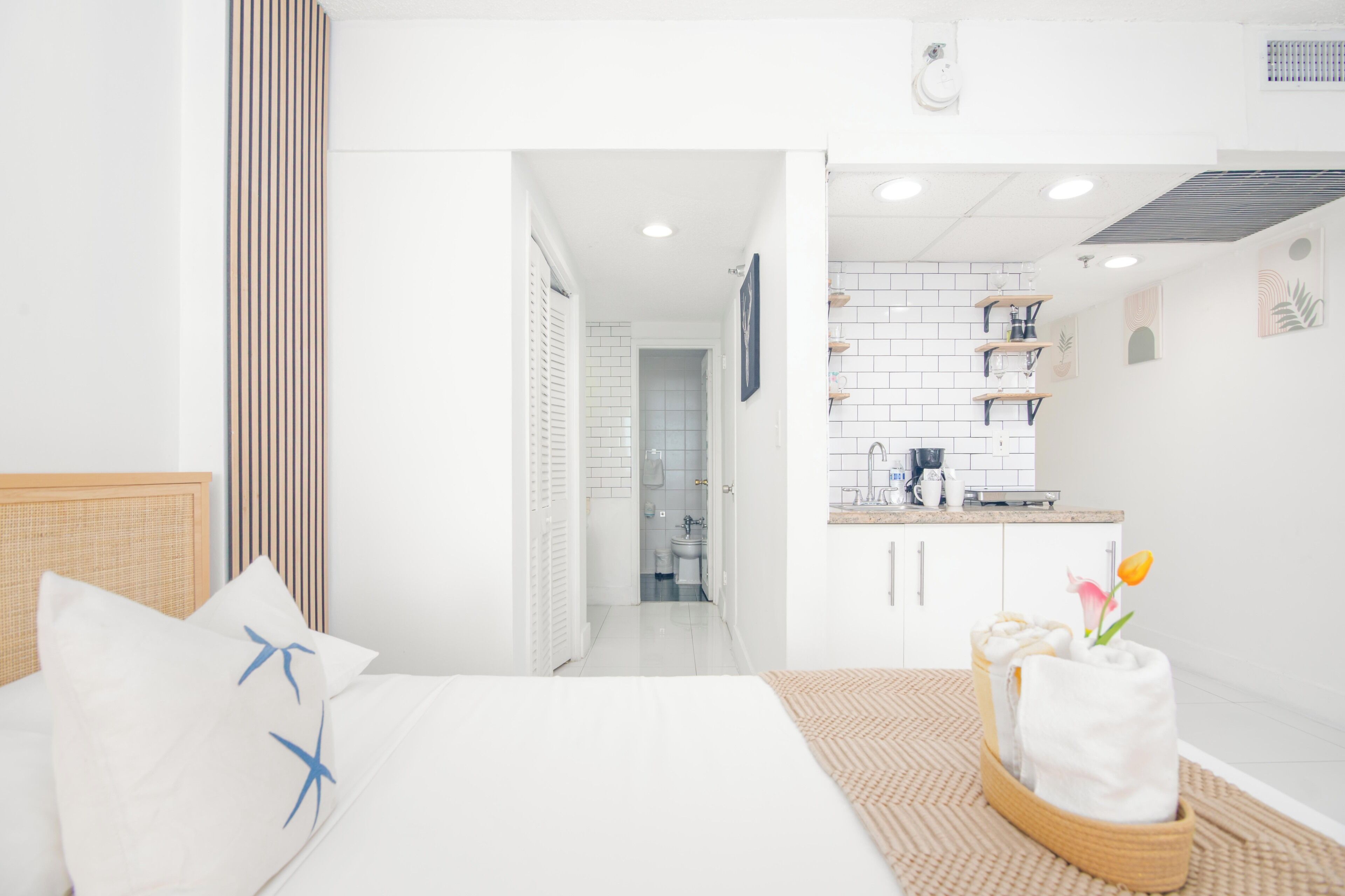 Una habitación de hotel moderna con una cama, una pequeña kitchenette y un baño visible a través de una puerta abierta.