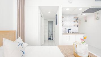 Una habitación de hotel moderna con una cama, una pequeña kitchenette y un baño visible a través de una puerta abierta.