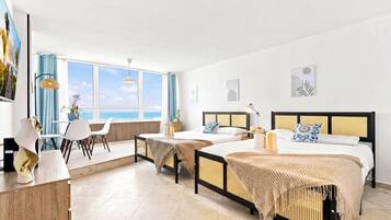 Quarto de hotel com duas camas, área de refeições e vista para o mar.