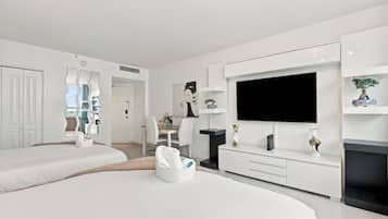 Una habitación de hotel moderna con dos camas, una zona de comedor, un televisor y un pequeño balcón.