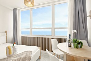A hotel room with a bed, a dining table, a chair, a potted plant, and a view of the sea. - Boutique Apartments Castle Beach (Miami Beach)