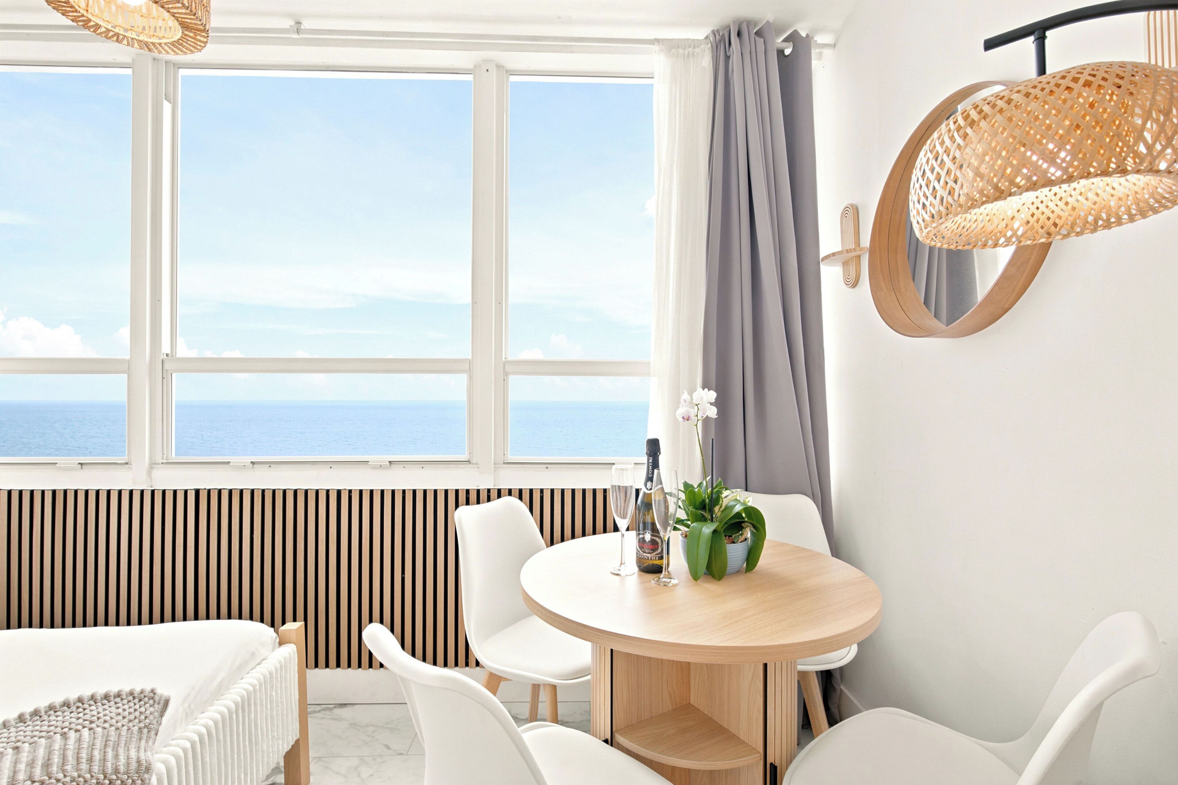 Een moderne kamer met een groot raam, een ronde houten tafel, witte stoelen, een potplant en een fles champagne.