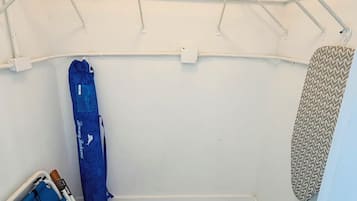 Uma área de lavanderia com varal, tábua de passar e uma sacola azul.