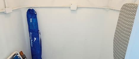 Un espace dédié à la lessive, équipé d’un étendoir, d’une planche à repasser et d’un sac bleu.