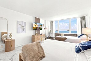 A hotel room with a large bed, a desk, a TV, and a view of the sea. - Boutique Apartments Castle Beach (Miami Beach)