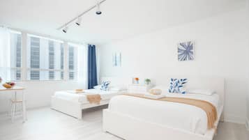 Quarto de hotel moderno com uma cama grande, uma cama menor, uma escrivaninha e uma janela com cortinas.