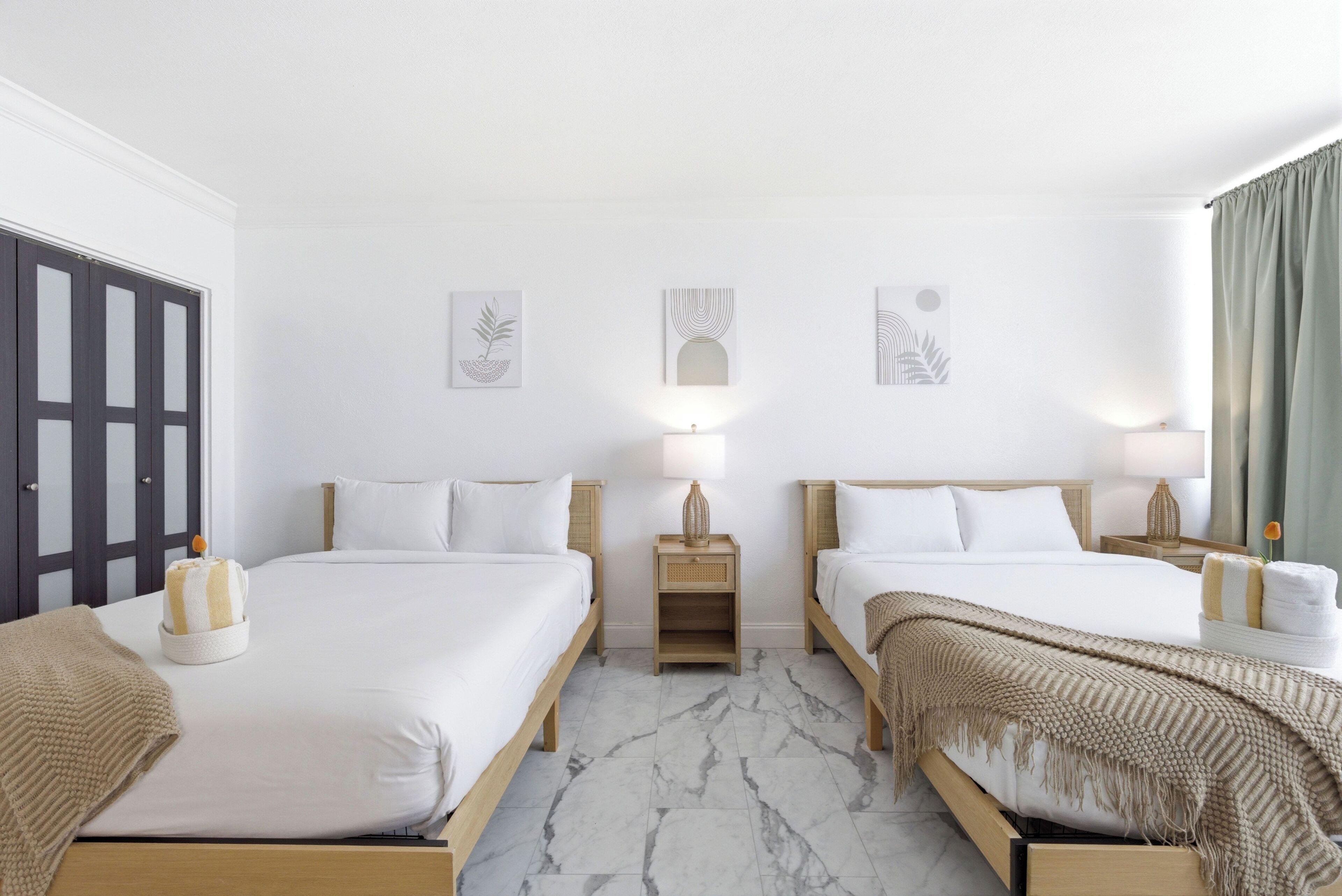 Habitación de hotel con dos camas, un armario, una mesita de noche con lámpara y decoración en la pared.
