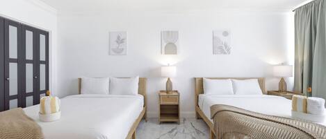 Una camera d'albergo con due letti, un armadio, un comodino con una lampada e opere d'arte alle pareti.