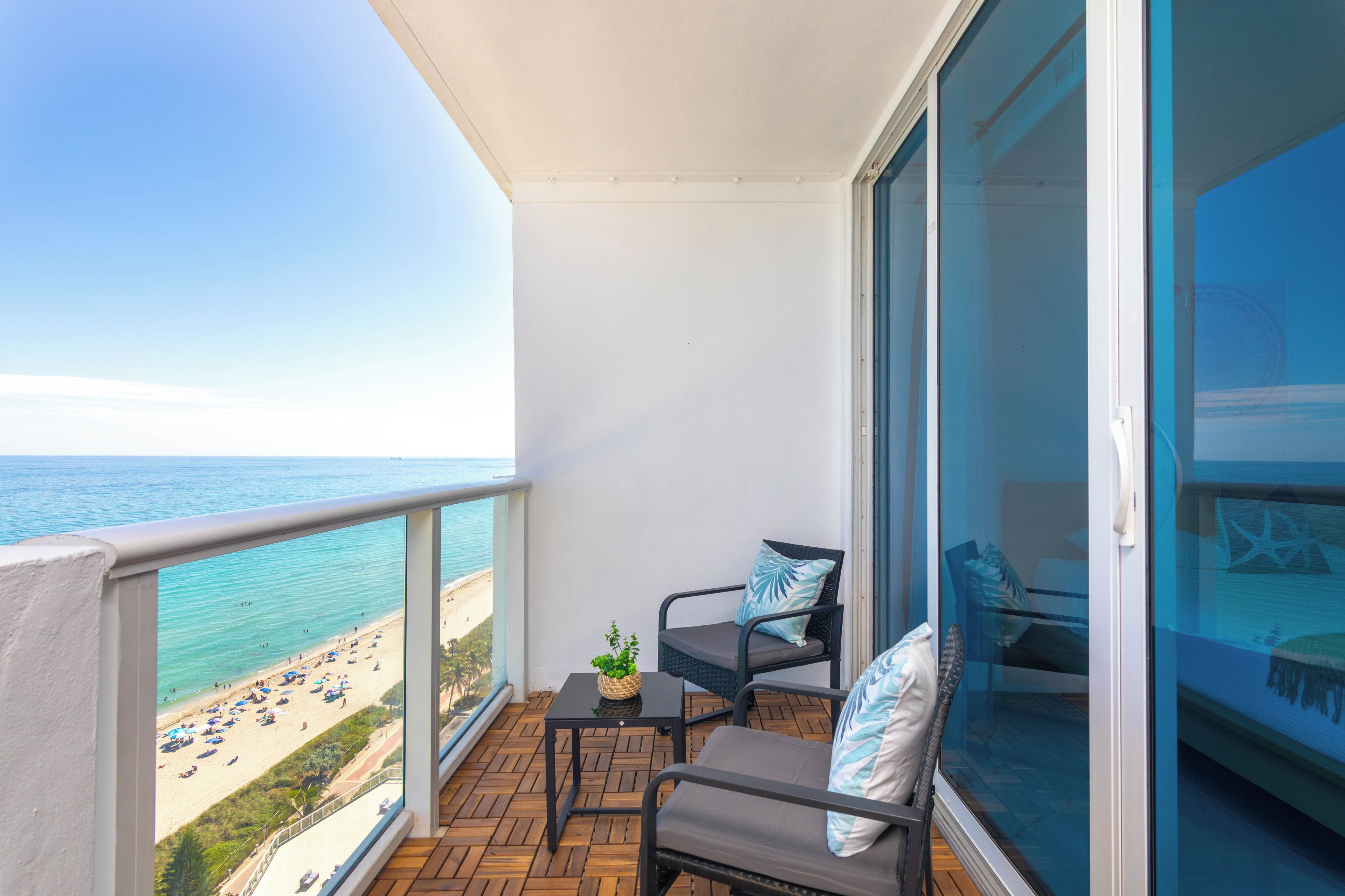 Een balkon met uitzicht op het strand, een tafel met stoelen en een potplant.