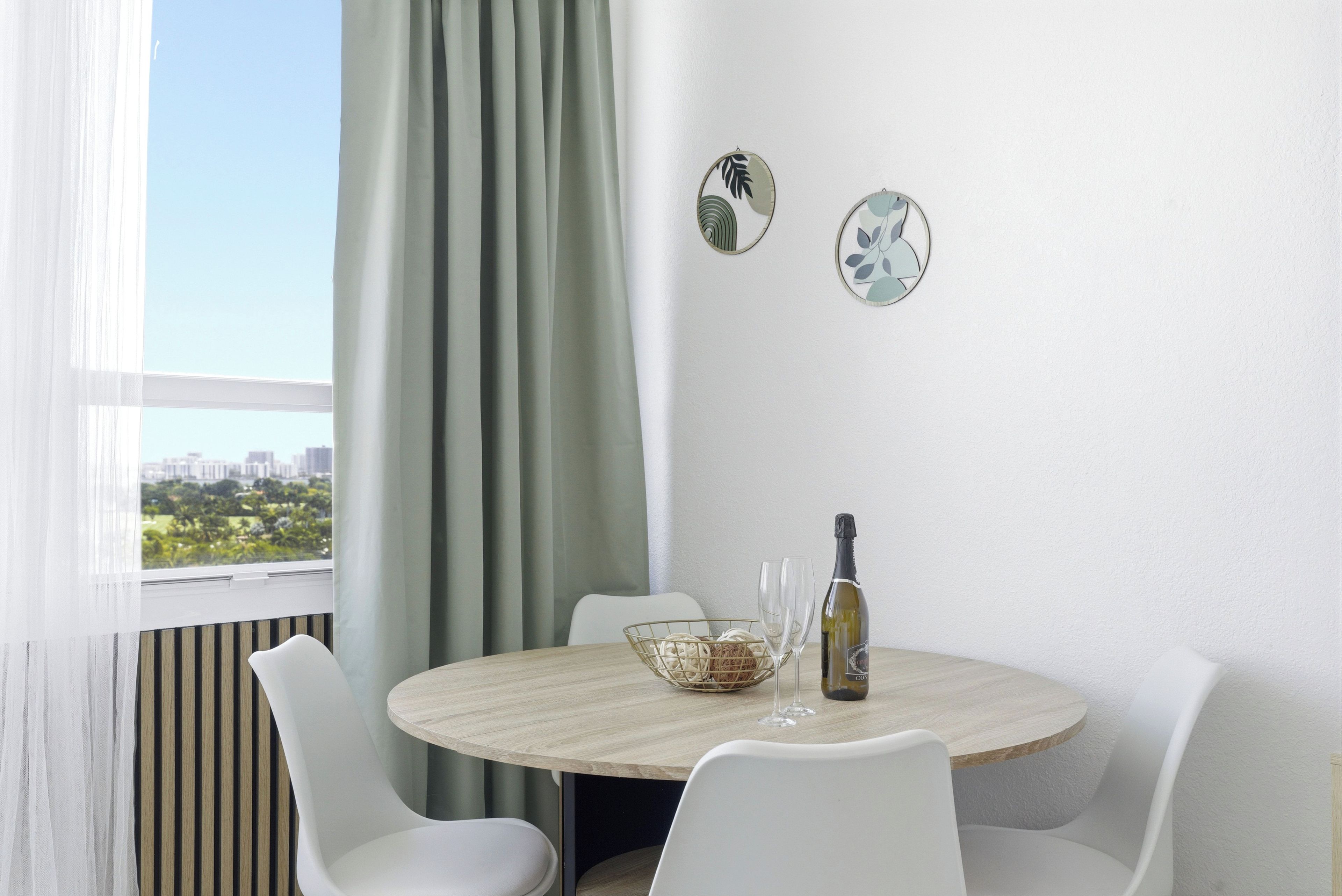 Un comedor moderno con una mesa redonda, sillas blancas, una botella de vino y platos decorativos en la pared.
