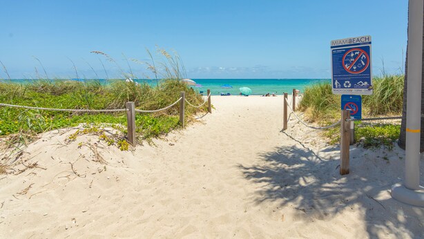 Un sentiero sulla spiaggia che conduce verso l'oceano, con un cartello che indica gli orari di chiusura.