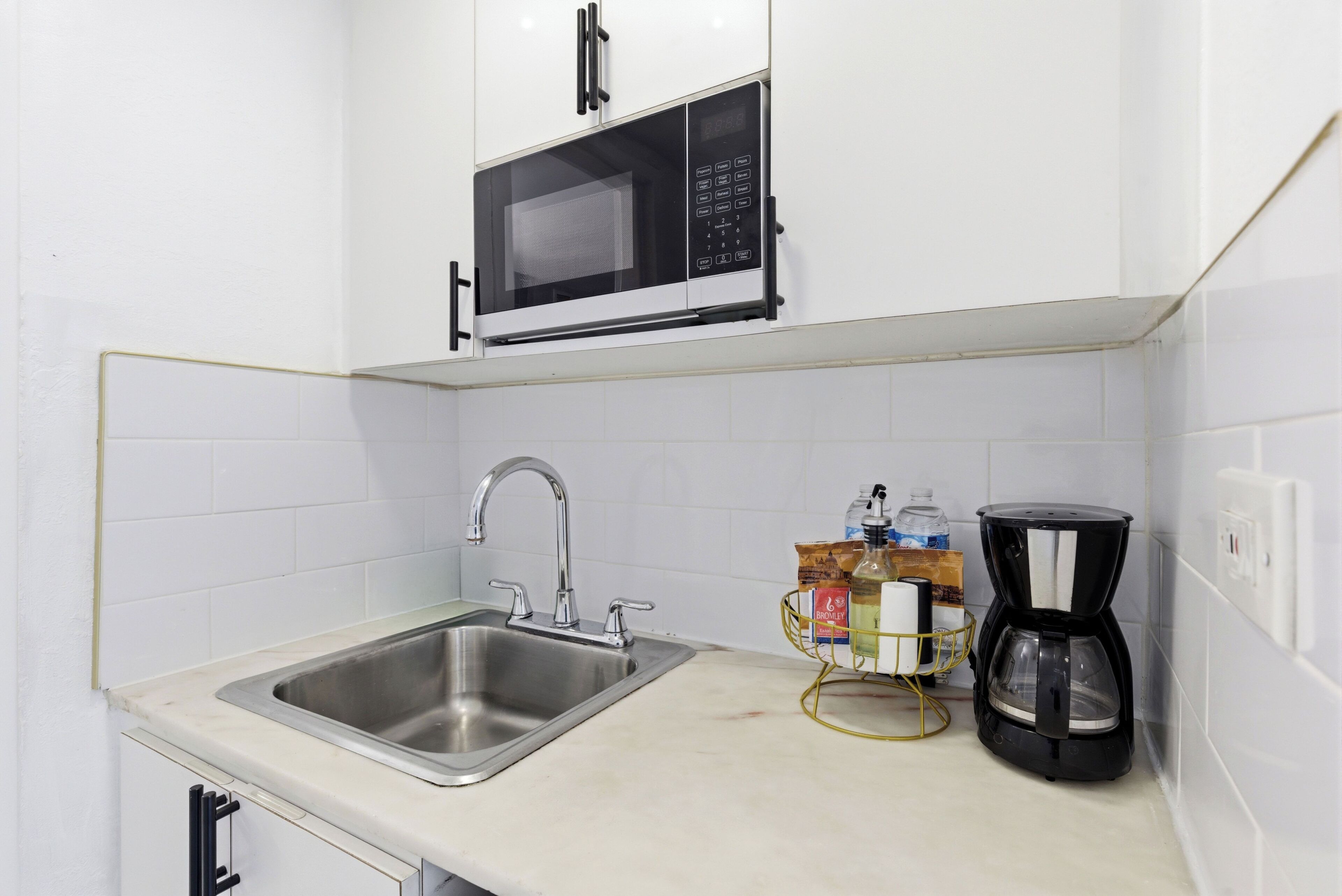 Een keuken met een roestvrijstalen spoelbak, een magnetron en een koffiezetapparaat.