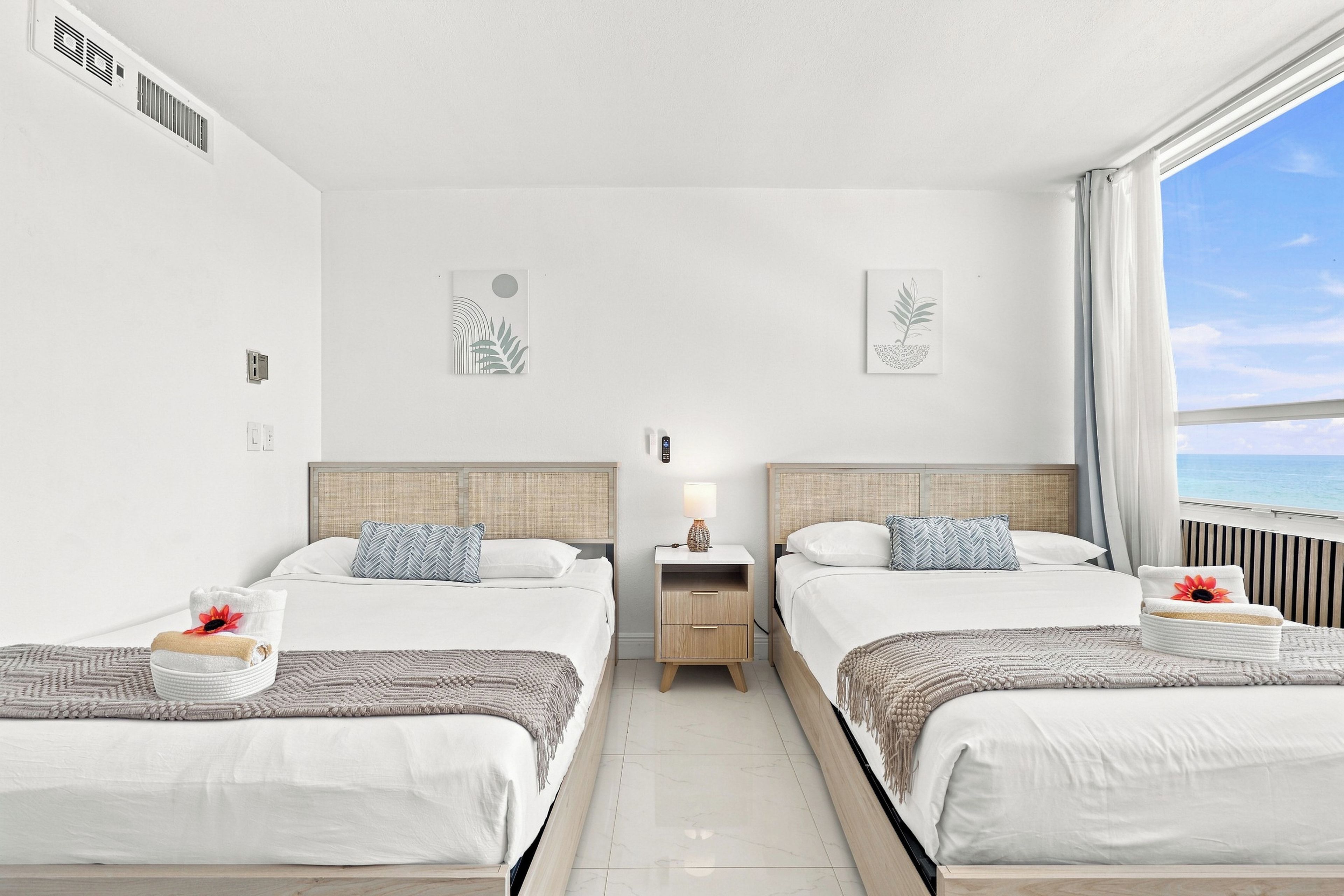 A hotel room with two beds, a nightstand, a lamp, and artwork on the walls.