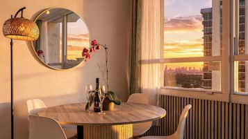 A dining area with a round table, chairs, a mirror, and a view of the city skyline at sunset.