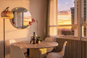 A dining area with a round table, chairs, a mirror, and a view of the city skyline at sunset. - Boutique Apartments Castle Beach (Miami Beach)