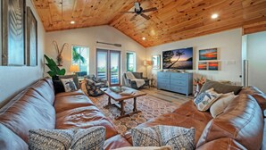 Ein geräumiges Wohnzimmer mit Holzboden, Ledersofas, einem Couchtisch und einem Fernseher.