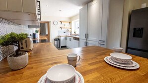 A modern kitchen with wooden countertops, white cabinets, and a dining area with a wooden table set for two. - Spacious 5-Bed Home with Views, Garden & Playroom (Silloth)