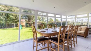 A dining area with a large table and chairs, large windows, and a view of a garden. - Spacious 5-Bed Home with Views, Garden & Playroom (Silloth)