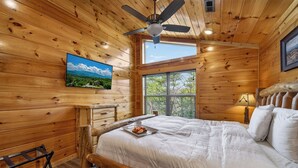 Ein Schlafzimmer einer Holzhütte mit einem Bett, einem Deckenventilator, einem Fenster und einem Bild an der Wand.