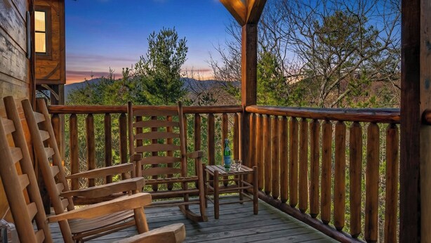 Eine Holzdar Terrasse mit Blick auf eine Berglandschaft, ein kleiner Tisch mit einer Flasche und zwei Holzstühle.
