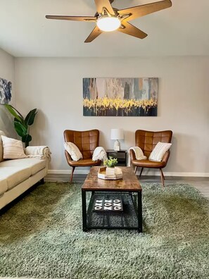 A living room with a ceiling fan, two leather armchairs, a wooden coffee table, a sofa, and a green shag rug.