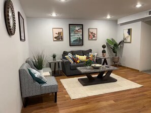 A living room with a sofa, armchair, coffee table, and decorative plants.