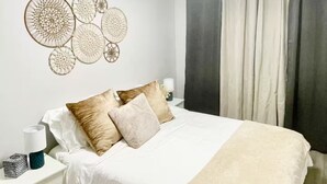 A neatly made bed with white bedding and two pillows, a bedside table with a lamp, and a wall decoration. - Home in Rochester-Mayo Clinic (Rochester)