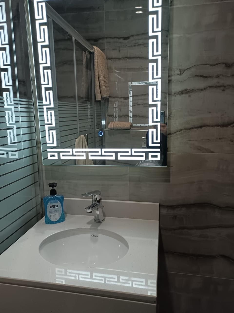 Une salle de bain dotée d’un meuble-lavabo moderne, d’un évier et d’un miroir encadré d’un motif géométrique.
