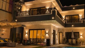 A modern two-story house with a swimming pool, outdoor seating, and a balcony.