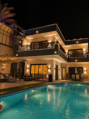 Una casa moderna de dos pisos con piscina, mobiliario exterior y un balcón.