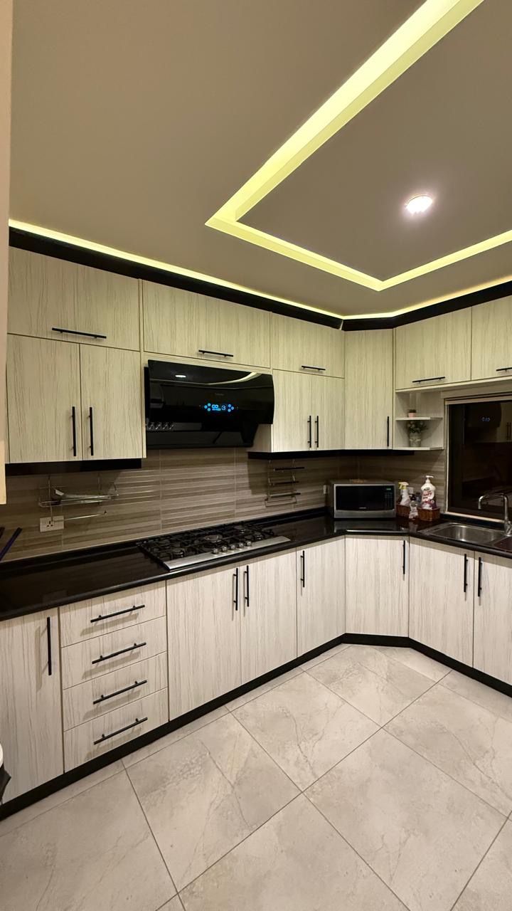 Een moderne keuken met lichte houten kastjes, een zwart aanrechtblad en een inbouwmagnetron.
