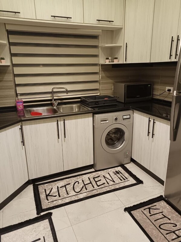 Una cocina compacta con lavadora, microondas y lavamanos.