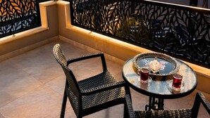 A balcony with a table and chairs, overlooking a cityscape at sunset.