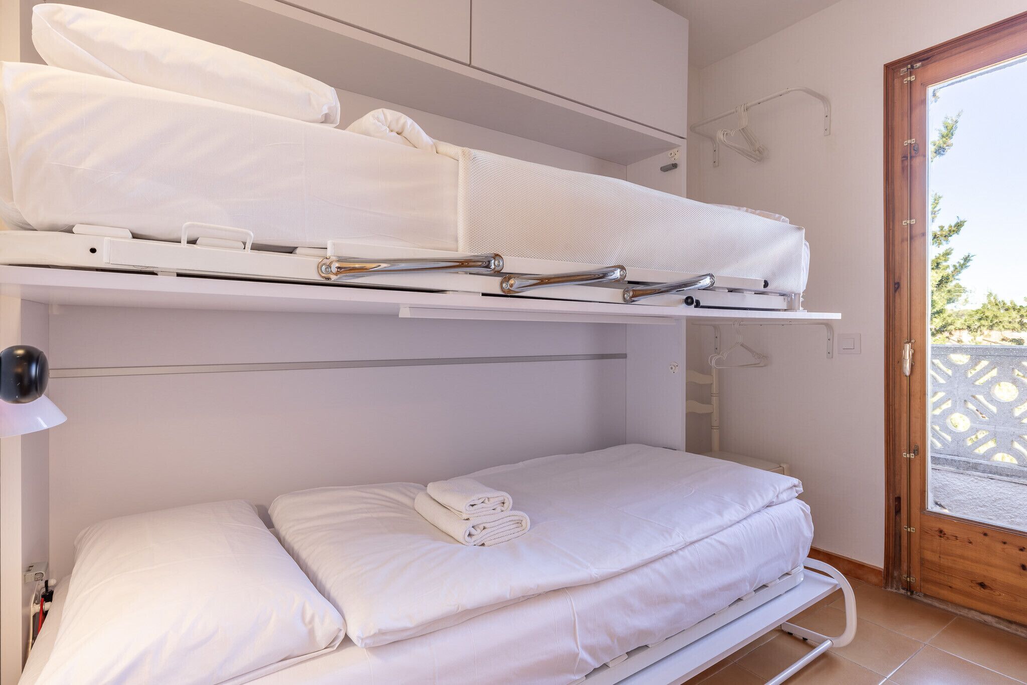Ein Zimmer mit einem Etagenbett, einem ausklappbaren Schreibtisch und einer Tür zu einem Außenbereich.