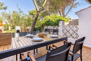 An outdoor dining area with a wooden table set for four, surrounded by chairs, and a view of a garden and building in the background. - Farigola house with communal pool (L'Escala)