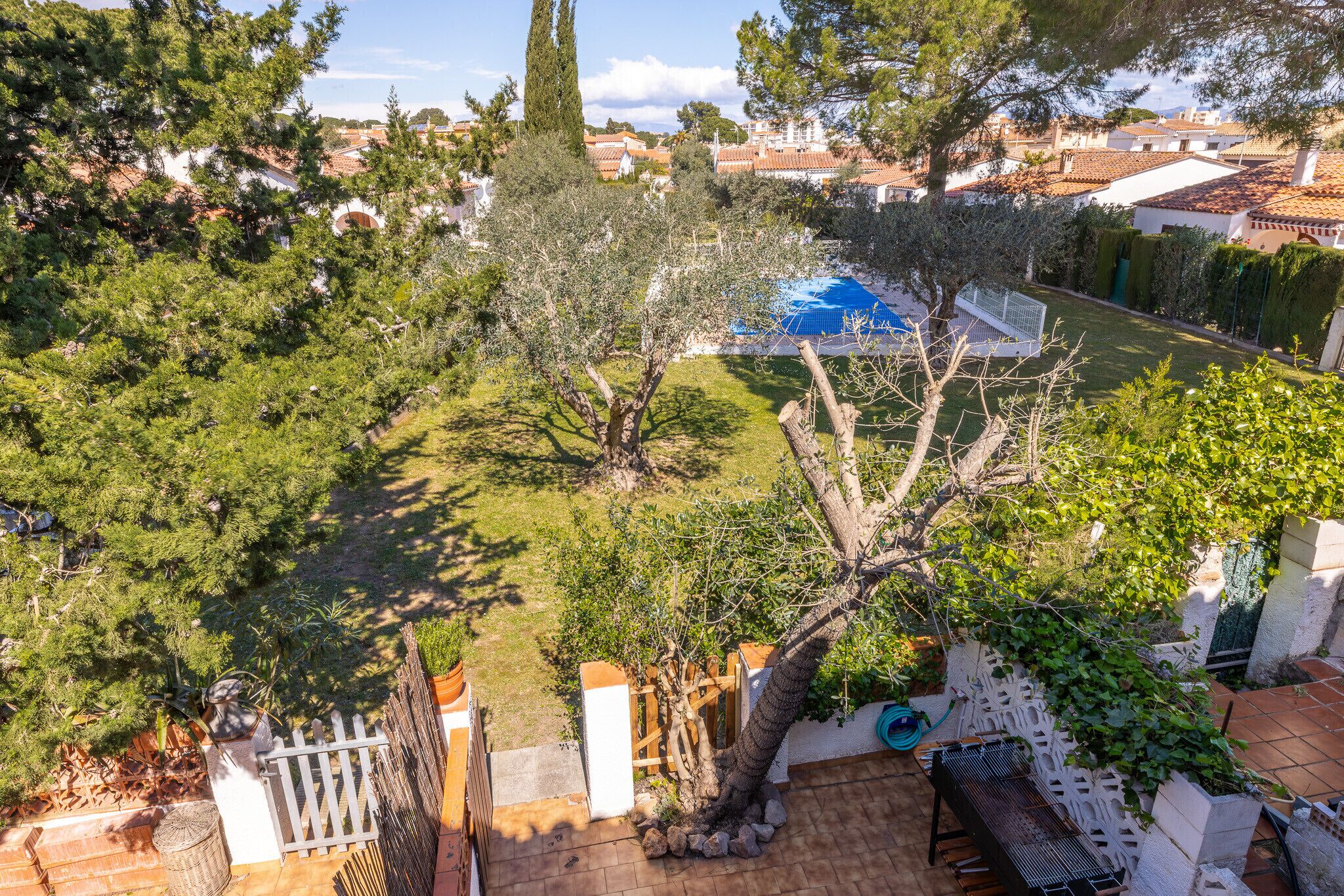 A residential area with a swimming pool, trees, and a white fence.
