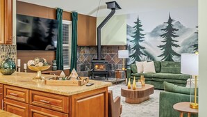 A modern kitchen with a central island, a built-in stove, and a large painting of a forest on the wall. - Forest Retreat • Theater • Full Spa • Speakeasy • GameRoom • MORE (East Stroudsburg)