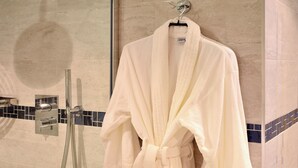Un peignoir blanc est accroché à un crochet dans un espace de douche clos par des parois de verre, dont l’un des murs est recouvert de carreaux.