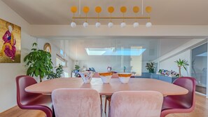 Een moderne eetruimte met een ronde tafel, roze stoelen en een plafondlamp.