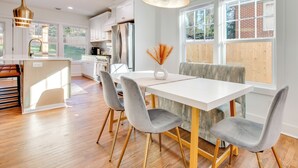 Una cucina moderna con mobili bianchi, un frigorifero in acciaio inossidabile e una zona pranzo con tavolo bianco e sedie grigie.