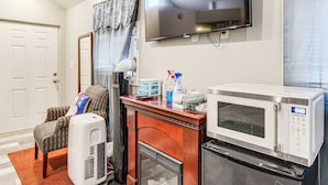 Un espace de vie compact comprenant un four à micro-ondes, un petit réfrigérateur, une cheminée, un téléviseur et un coin salon avec un fauteuil à motifs et un radiateur.