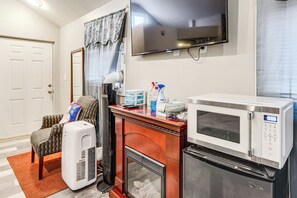 Ein kompakter Wohnbereich mit Mikrowelle, kleinem Kühlschrank, Kamin, Fernseher und einer Sitzecke mit einem gemusterten Sessel und einem Heizgerät.