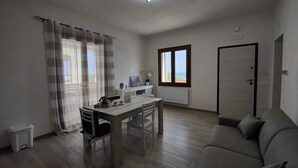 Ein modernes Wohnzimmer mit Holzboden, einer Couch, einem Esstisch mit Stühlen, einem Fenster mit Blick und einer Tür.