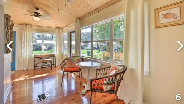A spacious room with wooden flooring, a ceiling fan, large windows, and a view of a garden. - Charming Home with Hot Tub and Garden, 20 minutes to Beach. (Palmetto)