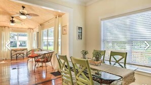 A dining area with a wooden table and chairs, a ceiling fan, and large windows with blinds. - Charming Home with Hot Tub and Garden, 20 minutes to Beach. (Palmetto)
