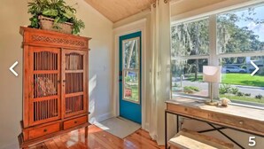 A room with a wooden cabinet, a blue door, a window with a view of the outside, and a lamp on a table. - Charming Home with Hot Tub and Garden, 20 minutes to Beach. (Palmetto)