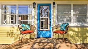 A yellow house with a blue door, two wicker chairs with red cushions, and a doormat. - Charming Home with Hot Tub and Garden, 20 minutes to Beach. (Palmetto)
